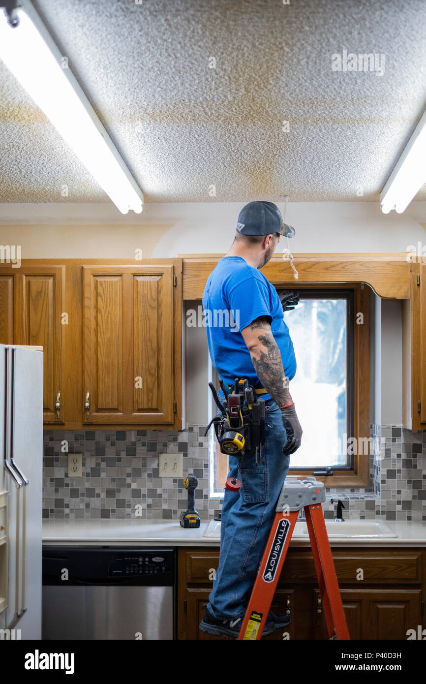 Uomo caucasico elettricista in piedi sulla scaletta e cambiare le luci di uscita durante una cucina rimodellare a Wichita, Kansas, Stati Uniti d'America. Foto Stock