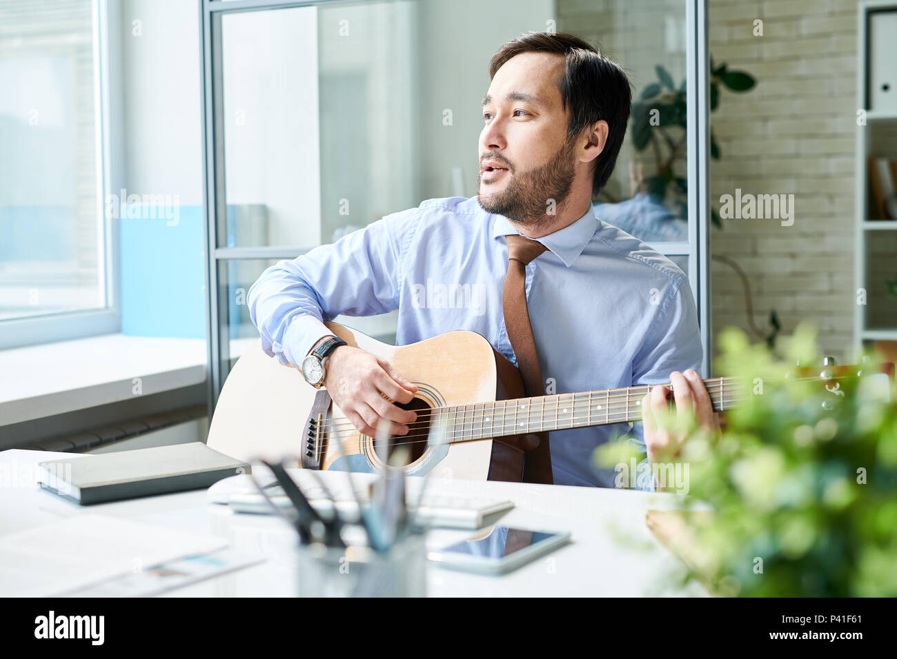 Uomo di contenuto a suonare la chitarra al lavoro Foto Stock