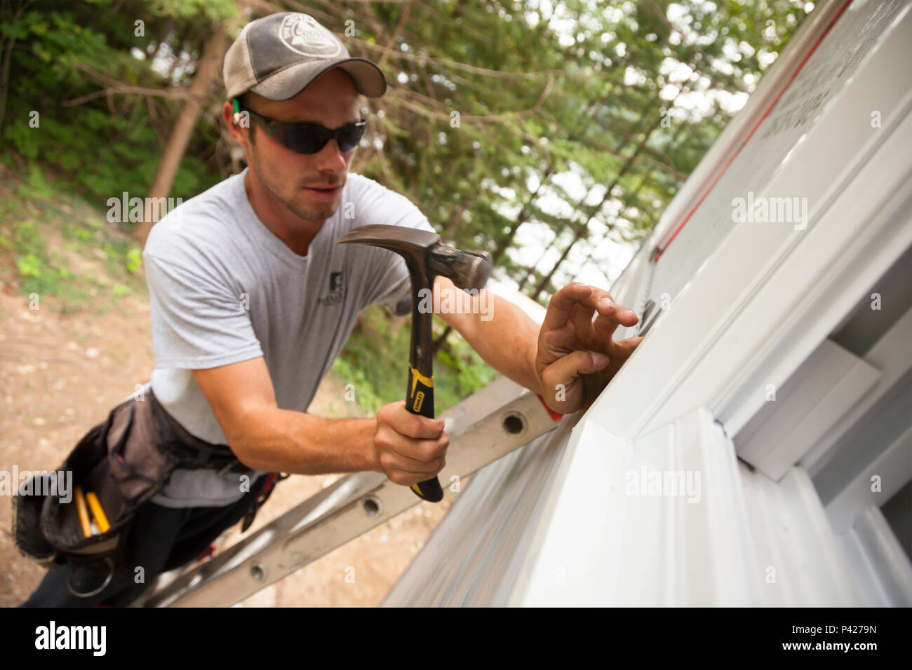 Un lavoratore edile martellare un chiodo per fissare il rivestimento di vinile in Ontario, Canada. Foto Stock