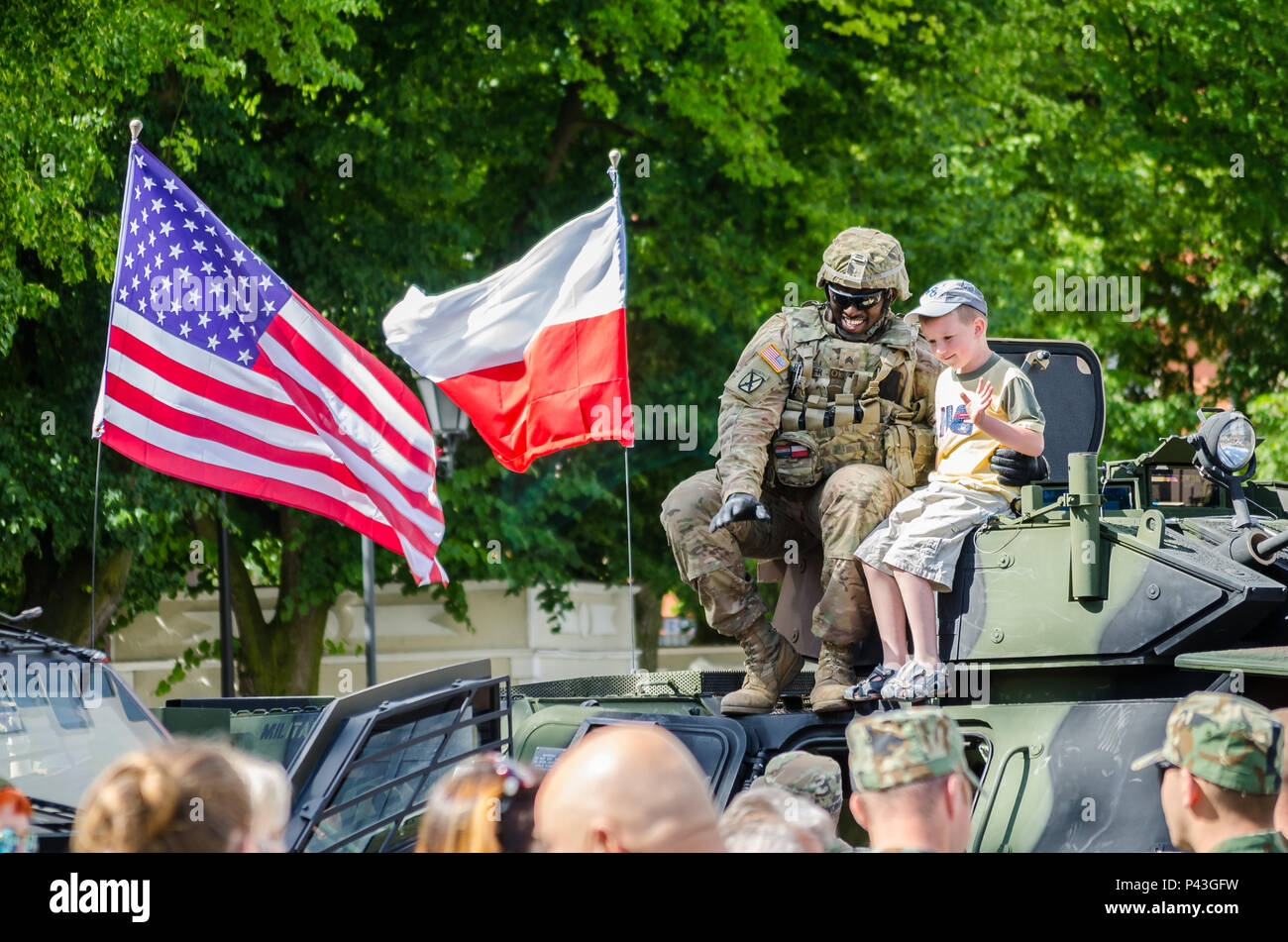 Un U.S. Soldato dell'esercito onde con un ragazzo polacco durante una giornata multiculturale in Chelmno, Polonia, 11 giugno 2016. Forze multinazionali hanno tenuto una visualizzazione di veicoli militari e ingranaggio nella piazza della città e da una parte di esercizio Anakonda 2016. Il polacco-led esercizio è un collettivo sforzo di formazione per rafforzare l'interoperabilità e rafforzare i legami tra le nazioni alleate e partner, collettivo per garantire la pace e la sicurezza nella regione. Foto Stock