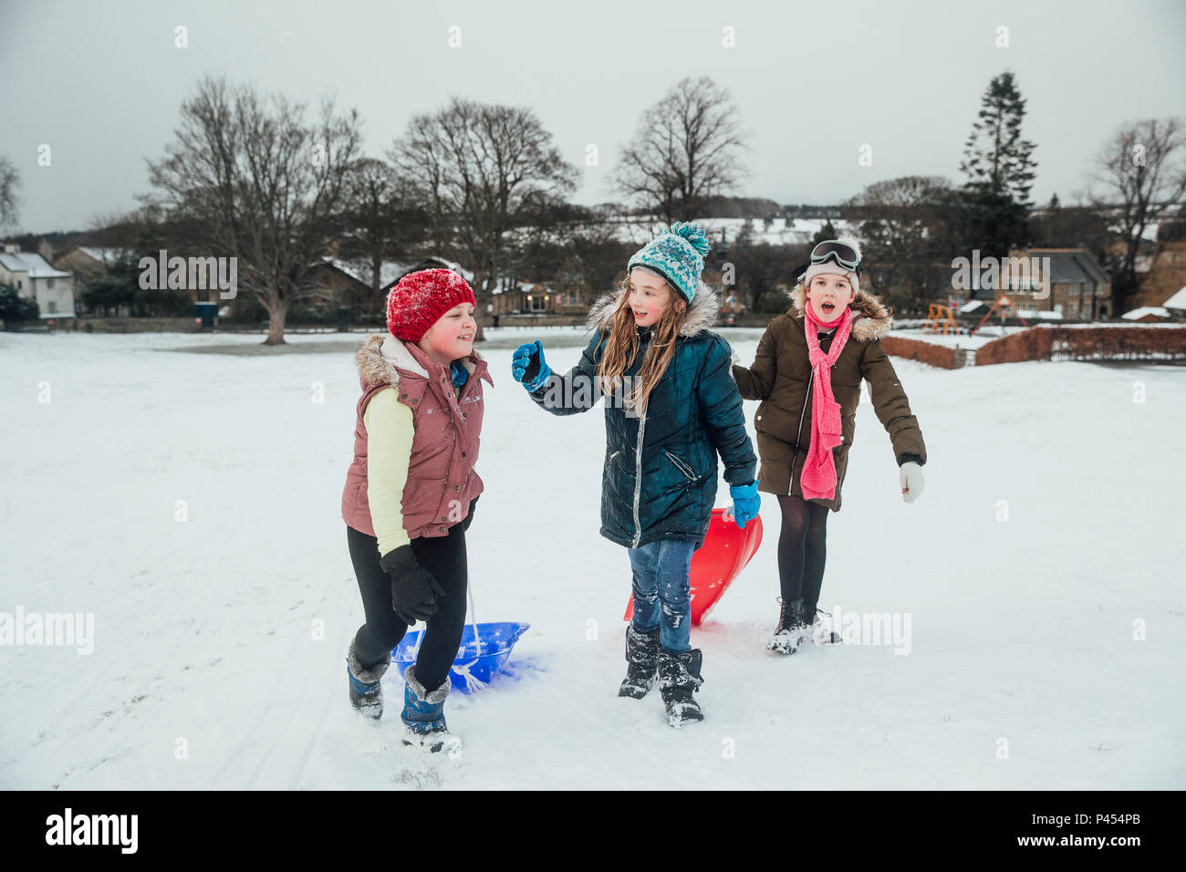 Tre bambine stanno parlando mentre sono fuori a giocare nella neve con slittini. Foto Stock