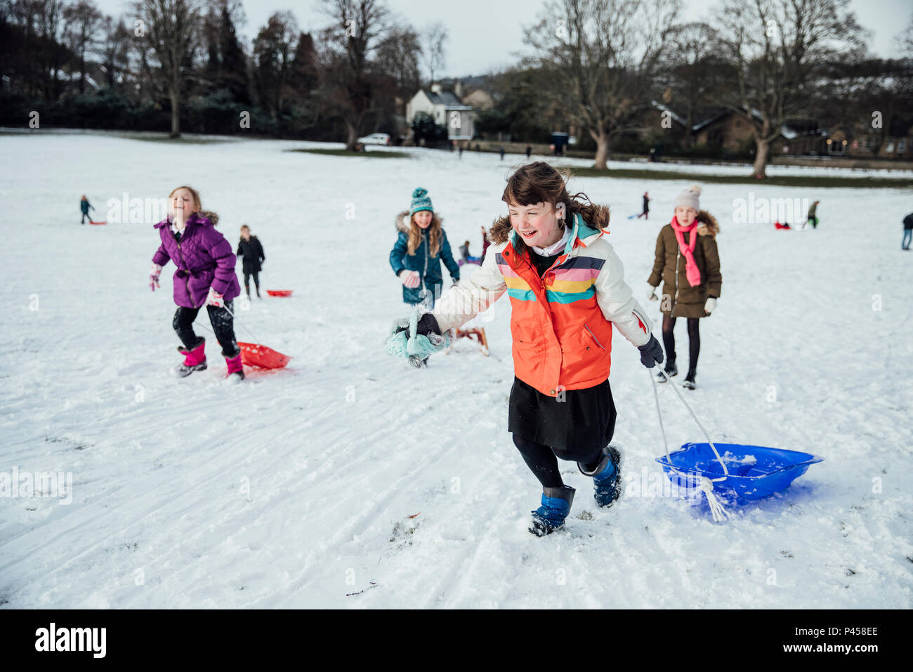 Gruppo di bambine sono in esecuzione fino alla cima di una collina nella neve per avere una gara di slitta. Foto Stock