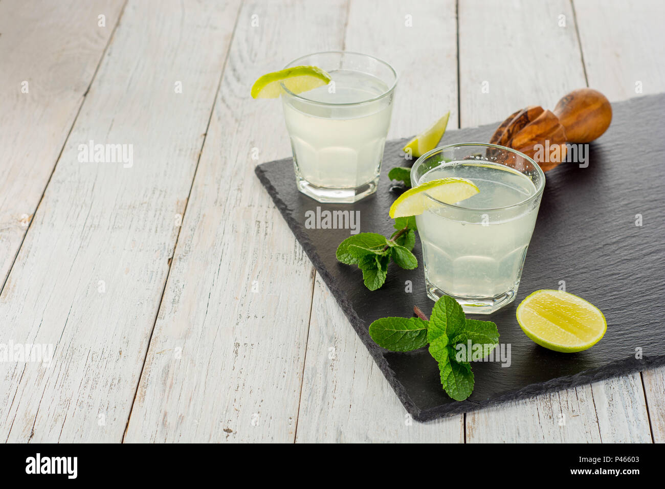 Bevanda estiva. Citrus limonata con la menta e il ghiaccio sul bianco sullo sfondo di legno. Foto Stock