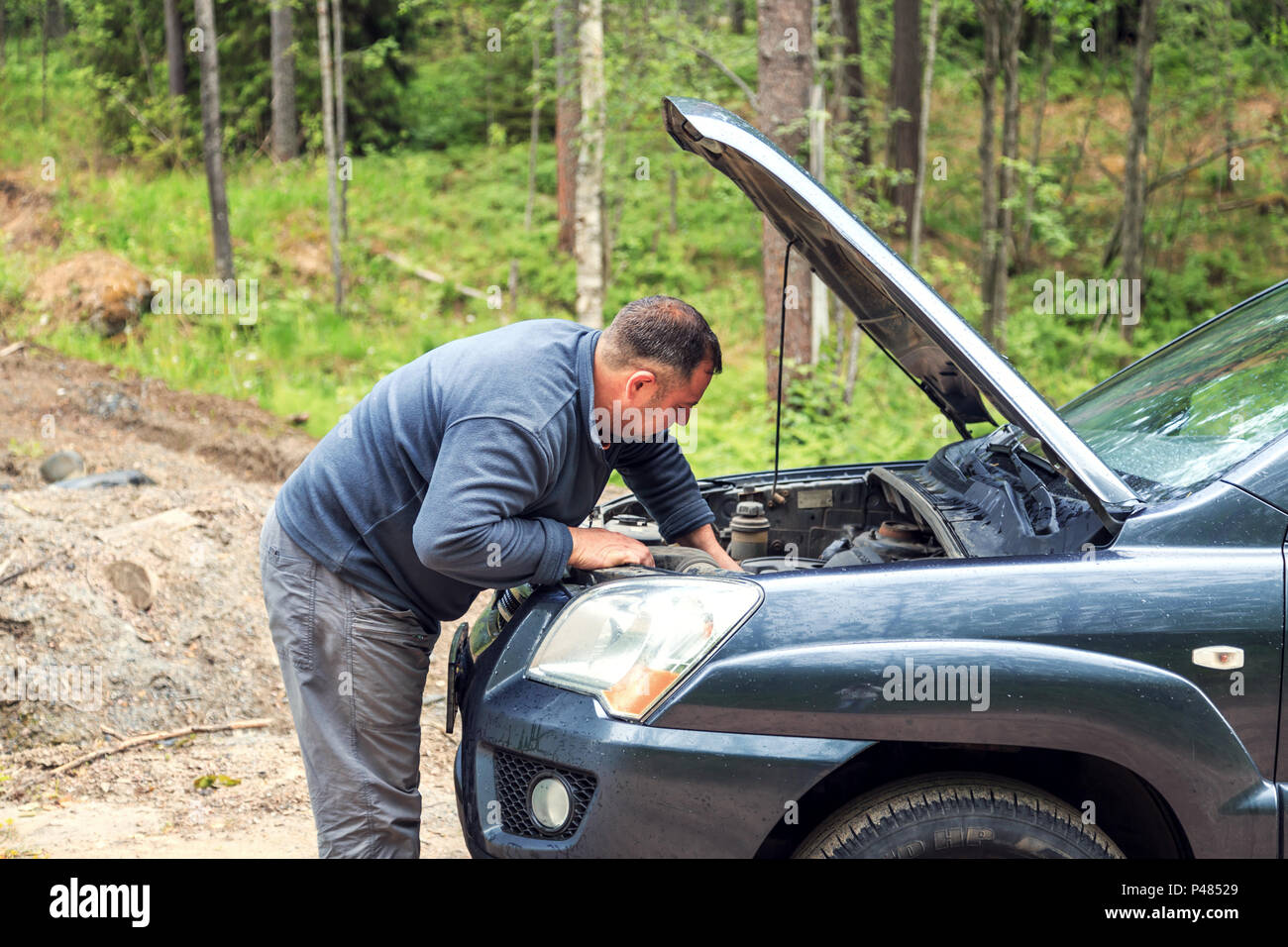 Stanco di riparazioni uomo rotto un auto. Strada della Foresta, Campagna. Foto Stock