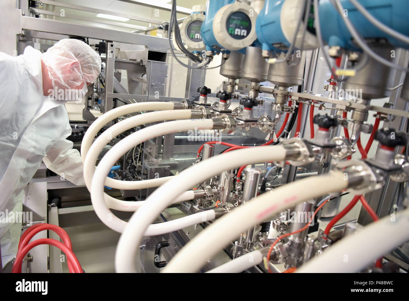 Lavoratore in sterili abbigliamento protettivo in una camera pulita di un pharamzie azienda opera l'impianto tecnico per la produzione di farmaci Foto Stock