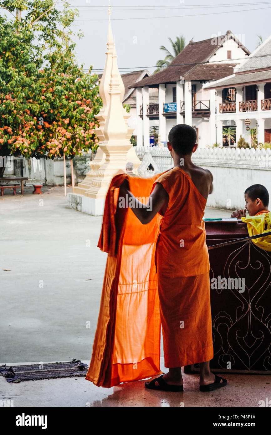 Luang Prabang o Louangphabang, Laos, sud-est asiatico : un laotiano monaco buddista si sparge fuori le vesti guardando verso alcuni stupa dall'Unesco H Foto Stock