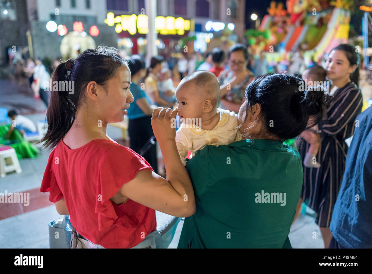 Madre e nonna godono di baby nel mezzo di vita notturna nella centrale piazza della città, Libo, Guizhou, Cina. Foto Stock