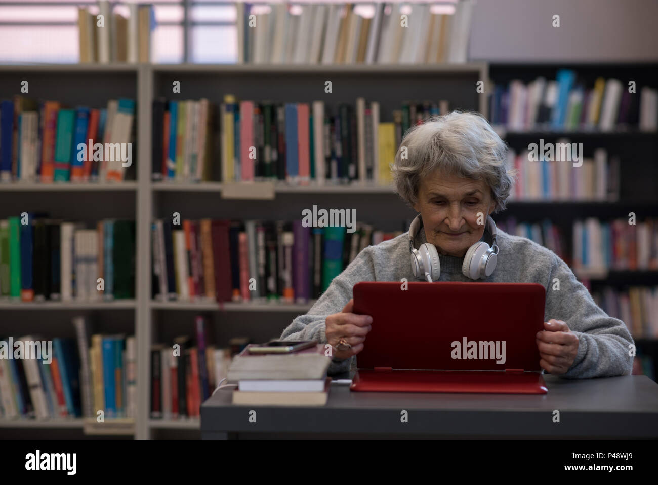 Senior donna utilizzando laptop in biblioteca Foto Stock