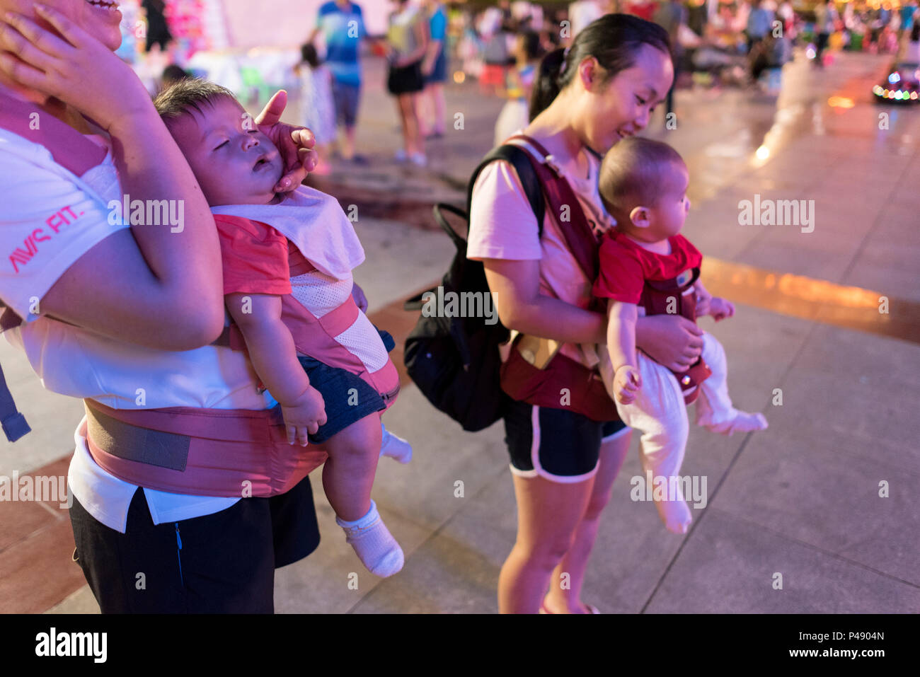 Due le mamme con bambini in vettori torace godetevi la vita notturna al city square sulla calda serata estiva, Libo, Guizhou, Cina. Foto Stock