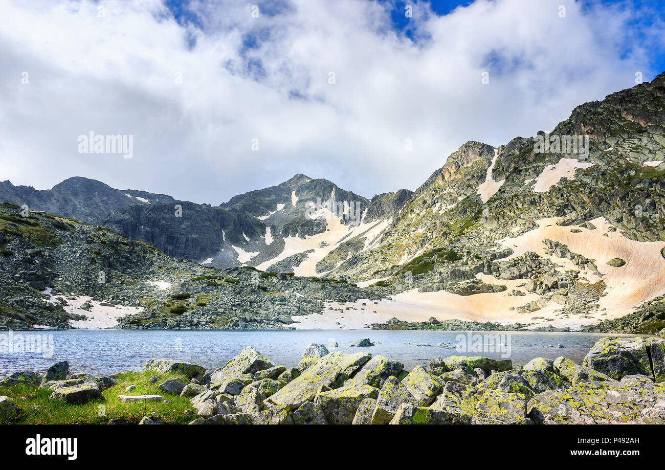 Montagna Rila lago e soleggiato Musala vertice su una coperta di neve paesaggio con rocce in primo piano Foto Stock