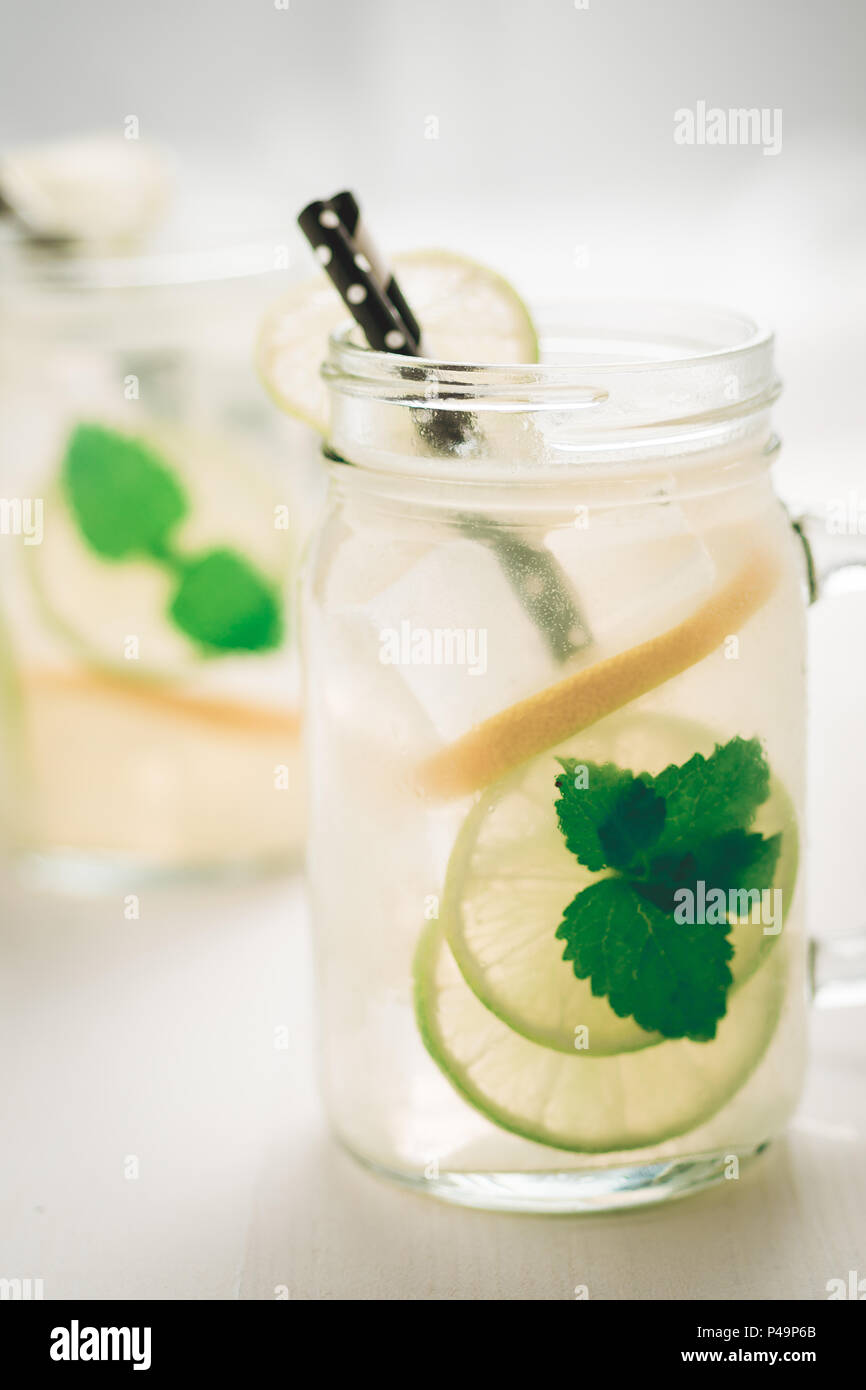 Freschi cocktail mojito con il ghiaccio freddo, limone e foglie di menta in Mason Jar sul legno bianco come sfondo luminoso il concetto di estate Foto Stock