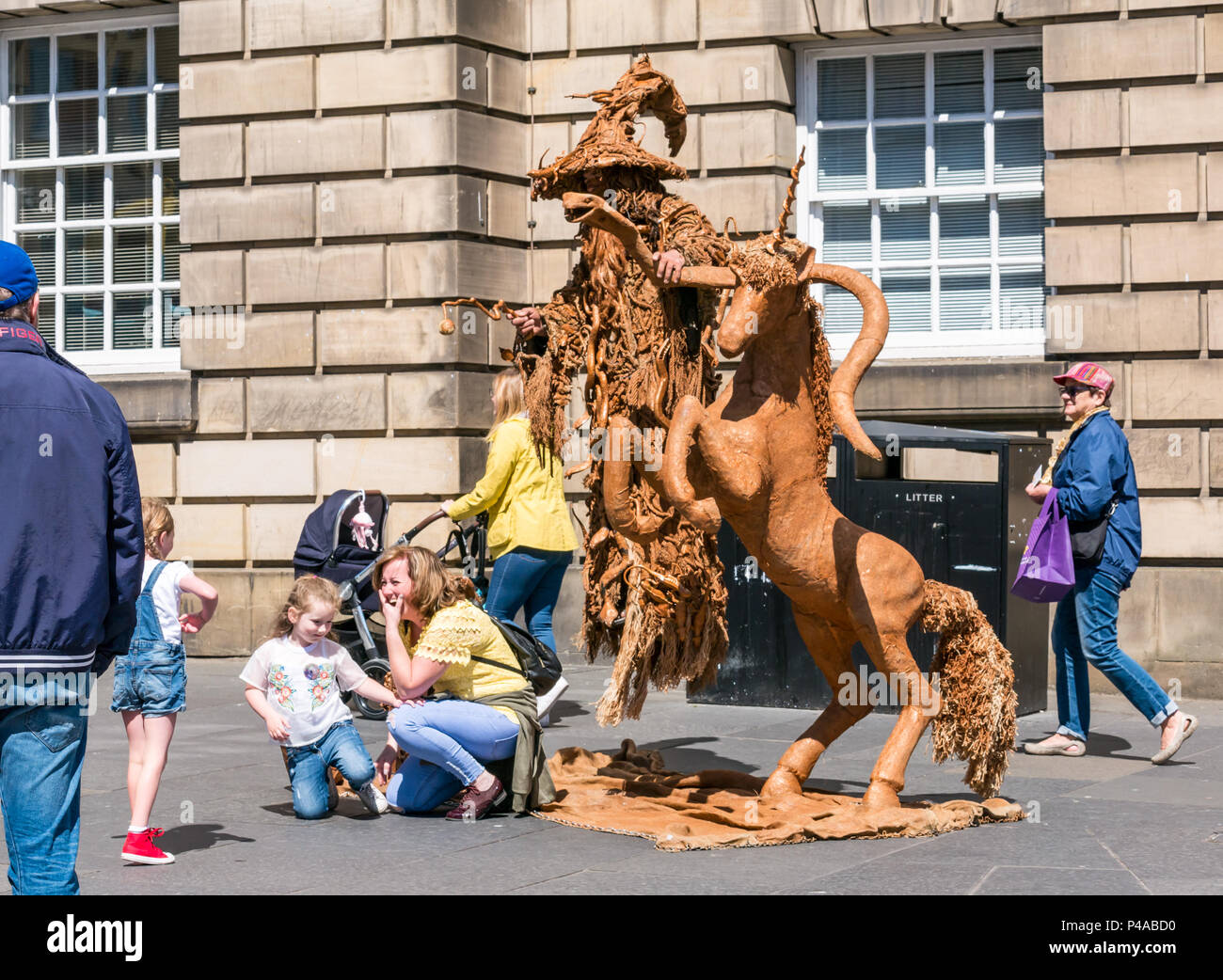 Edimburgo, Scozia, Regno Unito, 21 giugno 2018. Un esecutore di strada in un atto di levitazione vestito come Gandalf la procedura guidata con un liocorno per intrattenere i passanti sulla Royal Mile durante la stagione estiva. La donna e i bambini sono intrattenuti da strada agire come le persone passano da Foto Stock