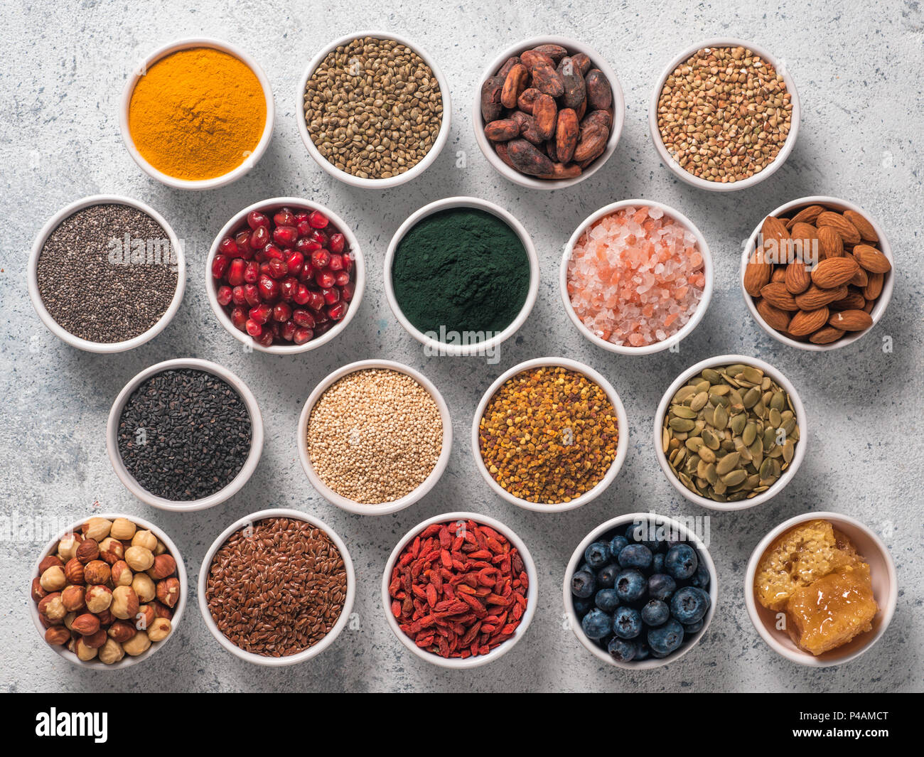 Varie superfoods nella piccola ciotola di cemento grigio Sfondo. Super come chia, spirulina, materie fava di cacao, goji, canapa, quinoa, polline di api, sesamo nero, curcuma. Vista superiore o flat-lay. Foto Stock