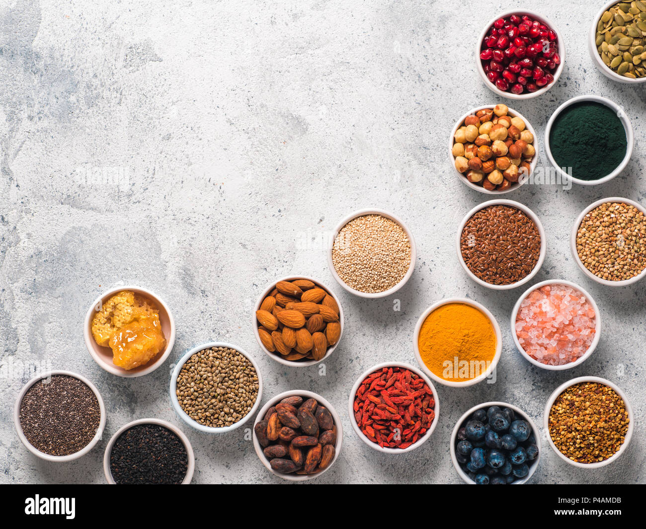 Varie superfoods nella piccola ciotola di cemento grigio Sfondo. Super come chia, spirulina, materie fava di cacao, goji, canapa, quinoa, polline di api, sesamo nero, curcuma. Copia spazio per il testo. Vista superiore, flat-lay. Foto Stock