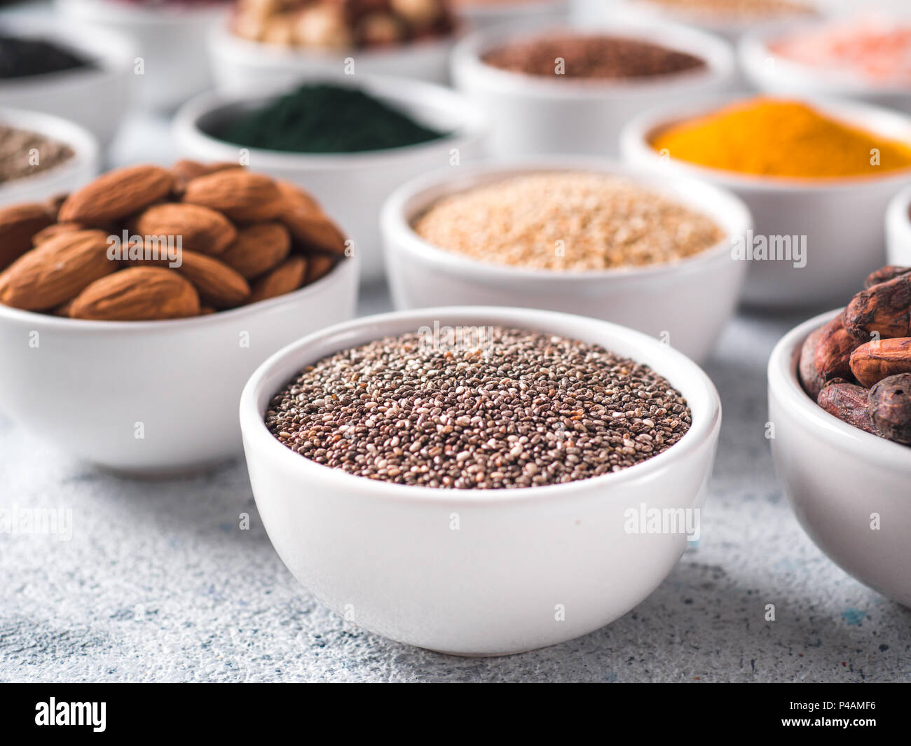 Semi di Chia in piccola ciotola bianco e altri superfoods sullo sfondo. Messa a fuoco selettiva. Superfoods diversi ingredienti. Concetto e illustrazione per la super e detox food Foto Stock