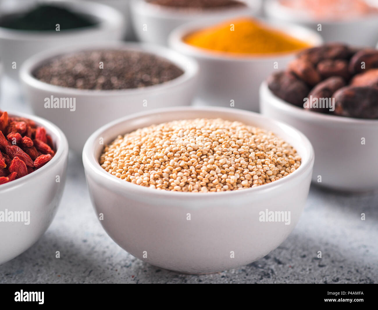 La quinoa in granella piccola ciotola bianco e altri superfoods sullo sfondo. Messa a fuoco selettiva. Superfoods diversi ingredienti. Concetto e illustrazione per la super e detox food Foto Stock