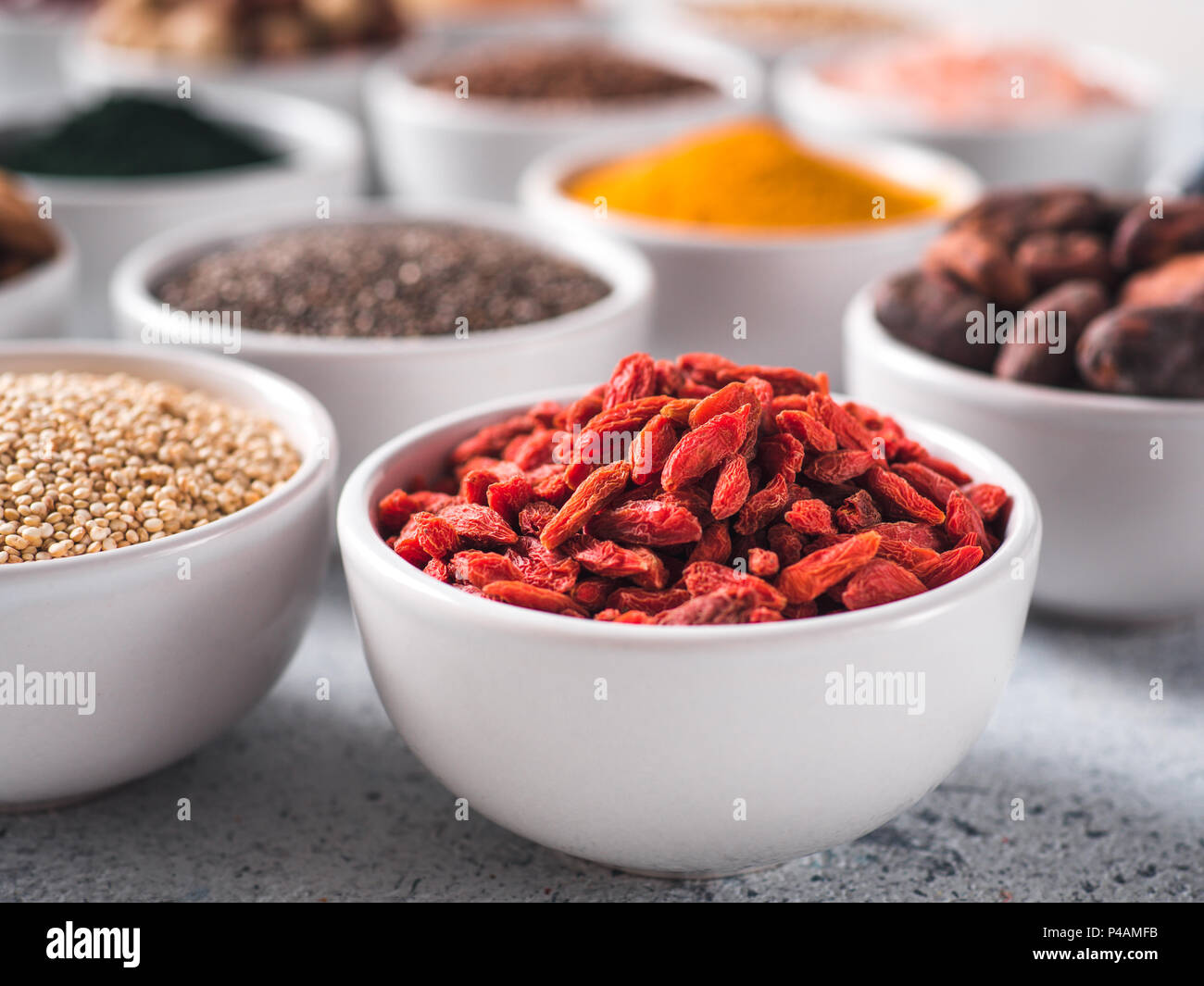 Bacche di Goji in piccola ciotola bianco e altri superfoods sullo sfondo. Messa a fuoco selettiva. Superfoods diversi ingredienti. Concetto e illustrazione per la super e detox food Foto Stock