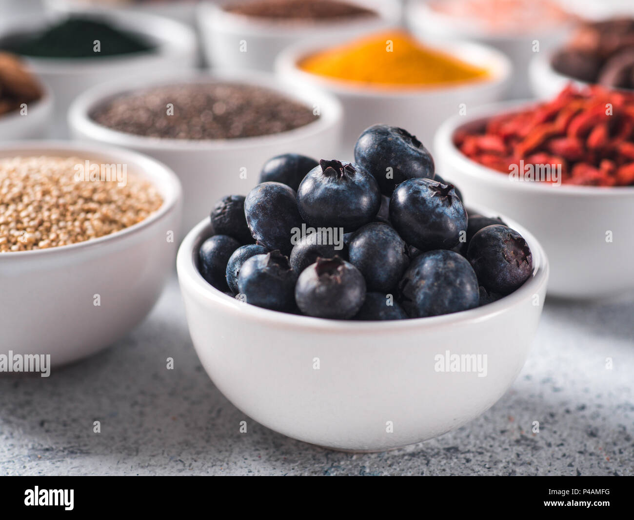 I mirtilli in piccola ciotola bianco e altri superfoods sullo sfondo. Messa a fuoco selettiva. Superfoods diversi ingredienti. Concetto e illustrazione per la super e detox food Foto Stock