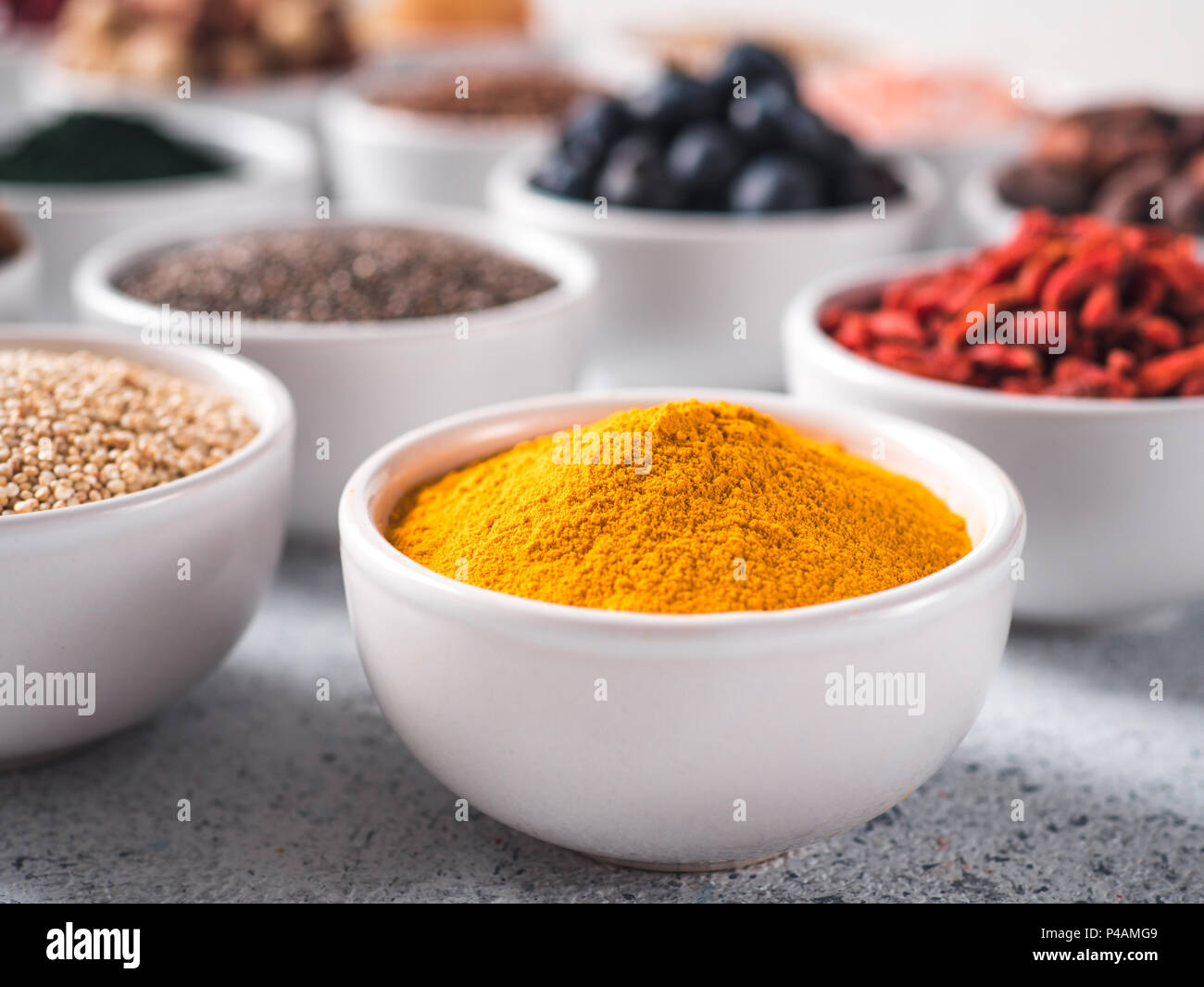 Curcuma in polvere nella piccola ciotola bianco e altri superfoods sullo sfondo. Messa a fuoco selettiva. Superfoods diversi ingredienti. Concetto e illustrazione per la super e detox food Foto Stock