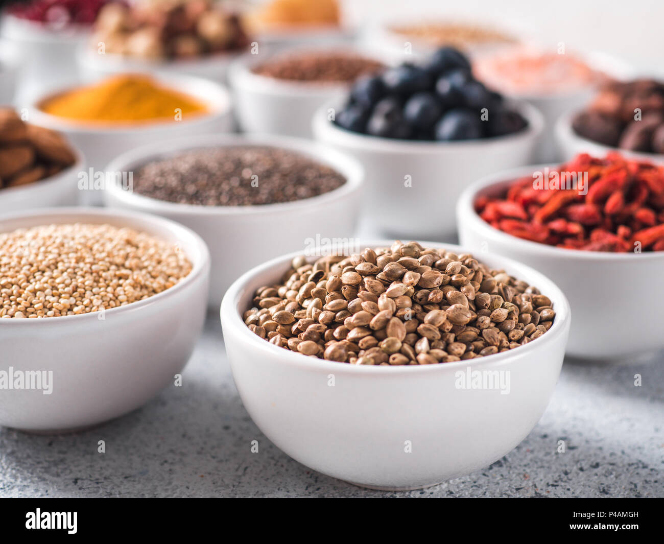 Sementi di canapa in piccola ciotola bianco e altri superfoods sullo sfondo. Messa a fuoco selettiva. Superfoods diversi ingredienti. Concetto e illustrazione per la super e detox food Foto Stock