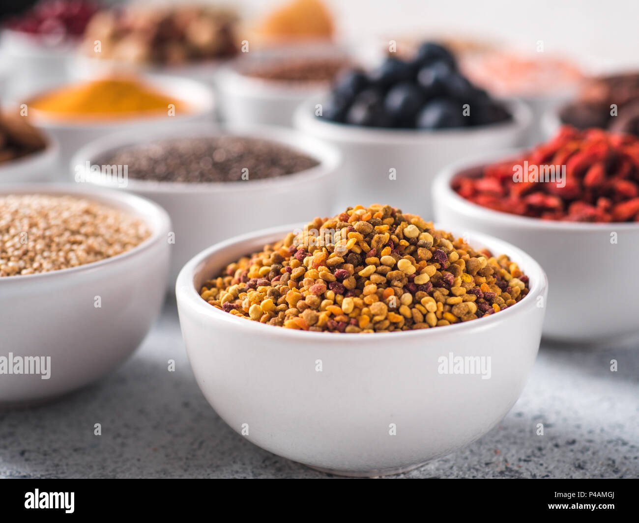 Polline di api o beebread in piccola ciotola bianco e altri superfoods sullo sfondo. Messa a fuoco selettiva. Superfoods diversi ingredienti. Concetto e illustrazione per la super e detox food Foto Stock