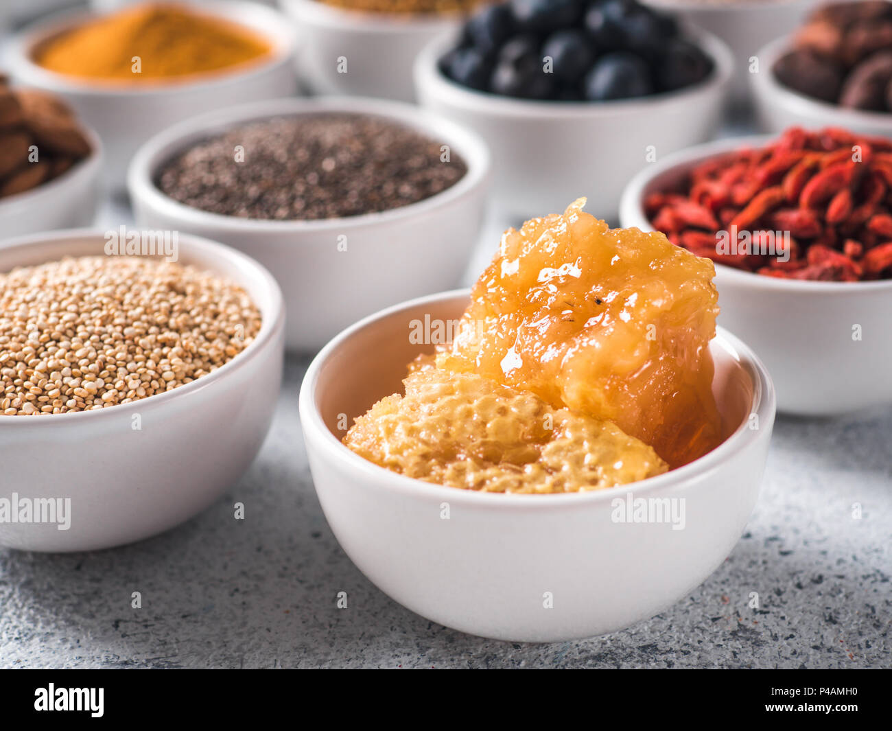 Hive o miele di favo di miele in piccola ciotola bianco e altri superfoods sullo sfondo. Messa a fuoco selettiva. Superfoods diversi ingredienti. Concetto e illustrazione per la super e detox food Foto Stock