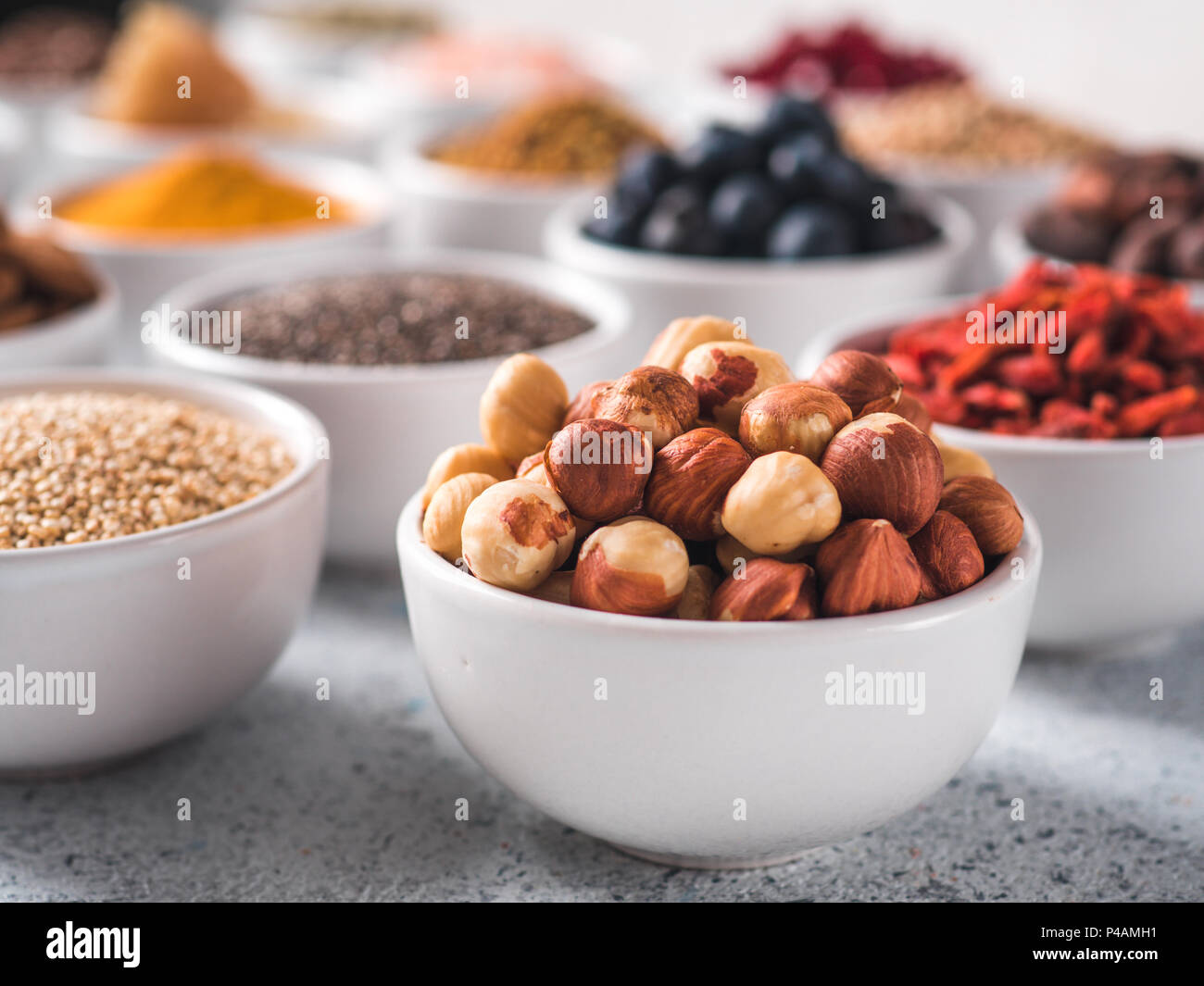 Nocciola nella piccola ciotola bianco e altri superfoods sullo sfondo. Messa a fuoco selettiva. Superfoods diversi ingredienti. Concetto e illustrazione per la super e detox food Foto Stock