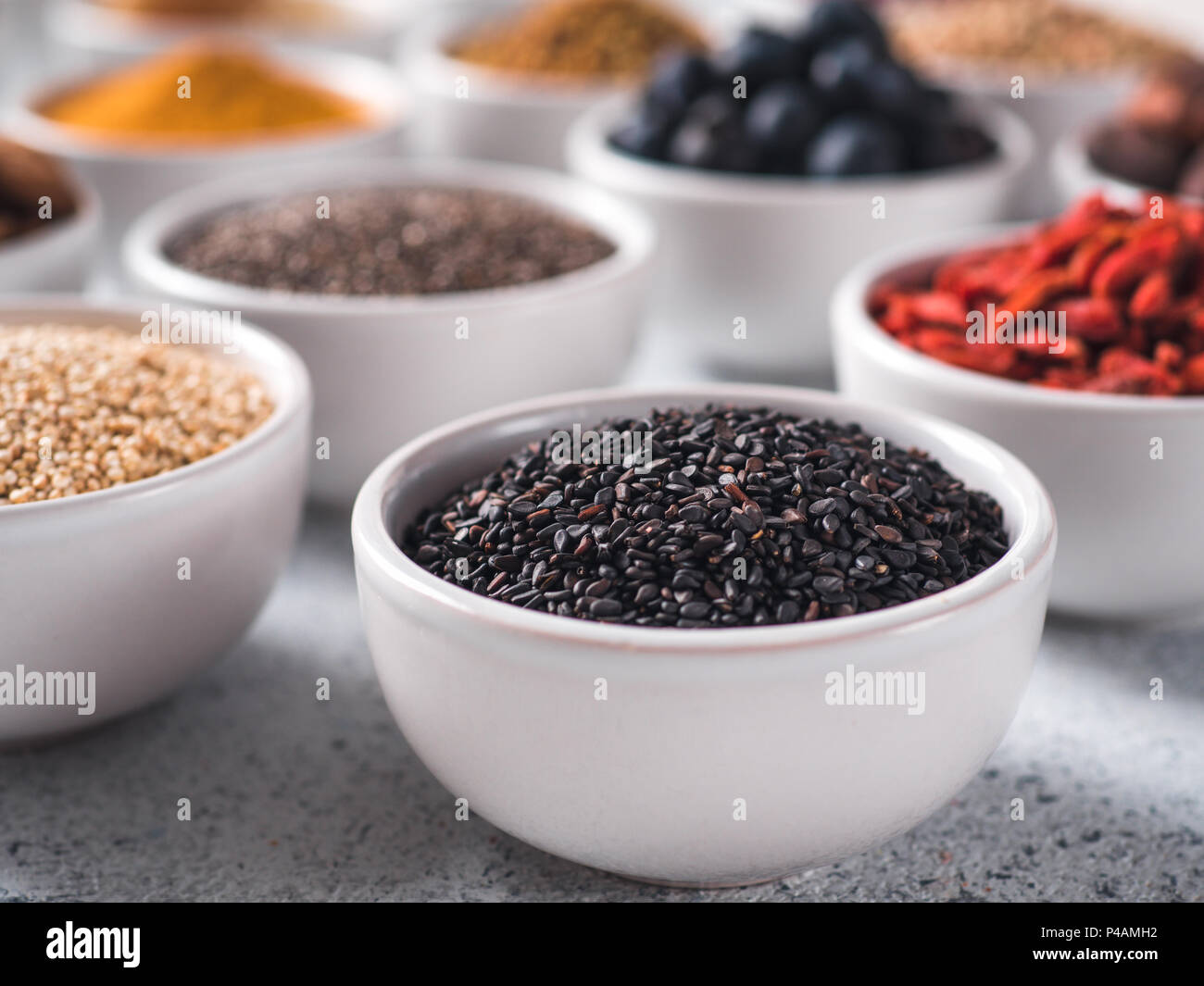 Sesamo nero in piccola ciotola bianco e altri superfoods sullo sfondo. Messa a fuoco selettiva. Superfoods diversi ingredienti. Concetto e illustrazione per la super e detox food Foto Stock
