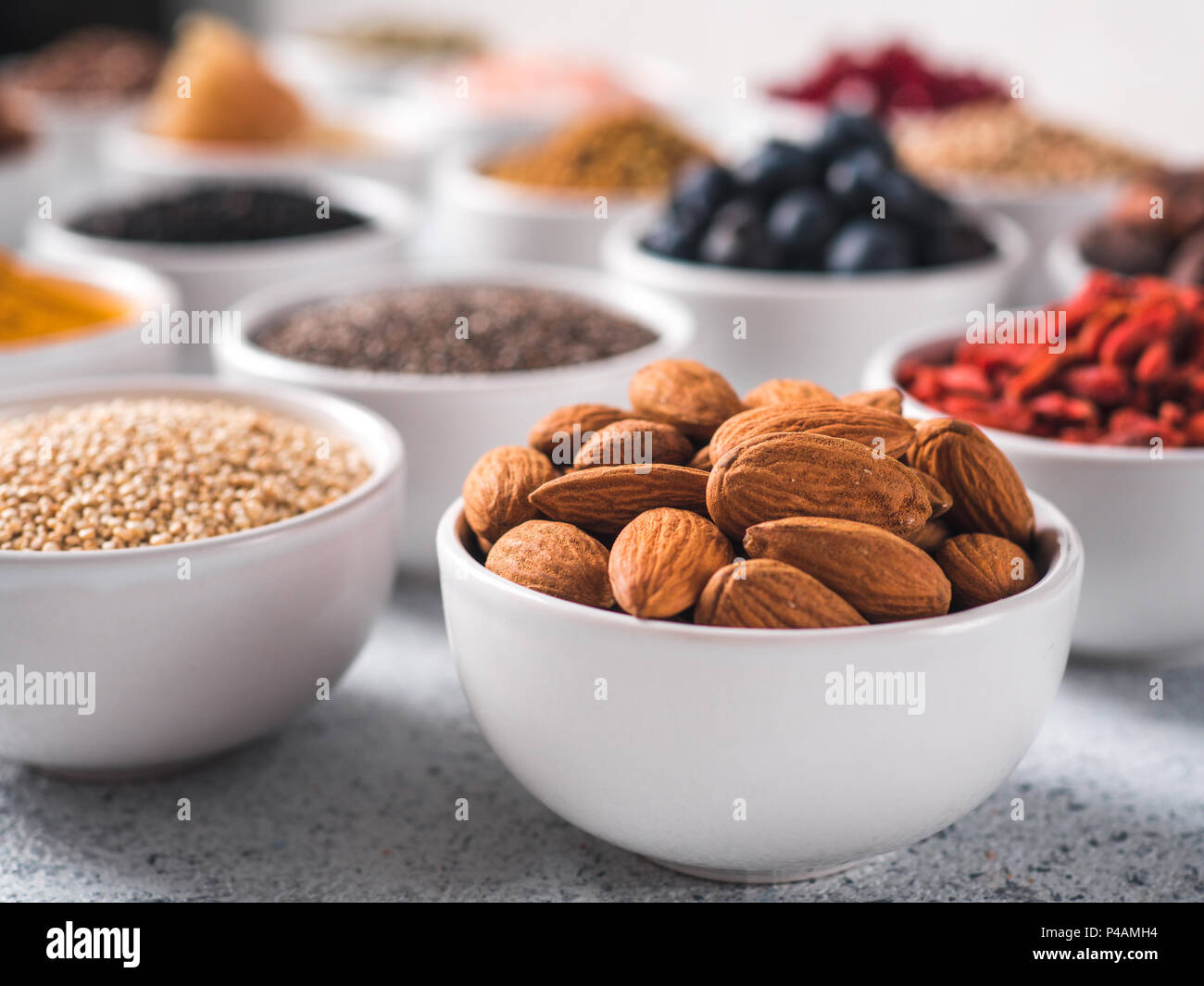 Mandorlo in piccola ciotola bianco e altri superfoods sullo sfondo. Messa a fuoco selettiva. Superfoods diversi ingredienti. Concetto e illustrazione per la super e detox food Foto Stock