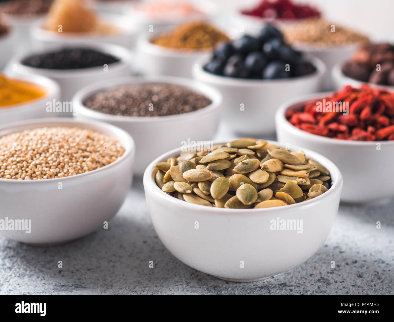 Materie pepitas o i semi di zucca in piccola ciotola bianco e altri superfoods sullo sfondo. Messa a fuoco selettiva. Superfoods diversi ingredienti. Concetto e illustrazione per la super e detox food Foto Stock