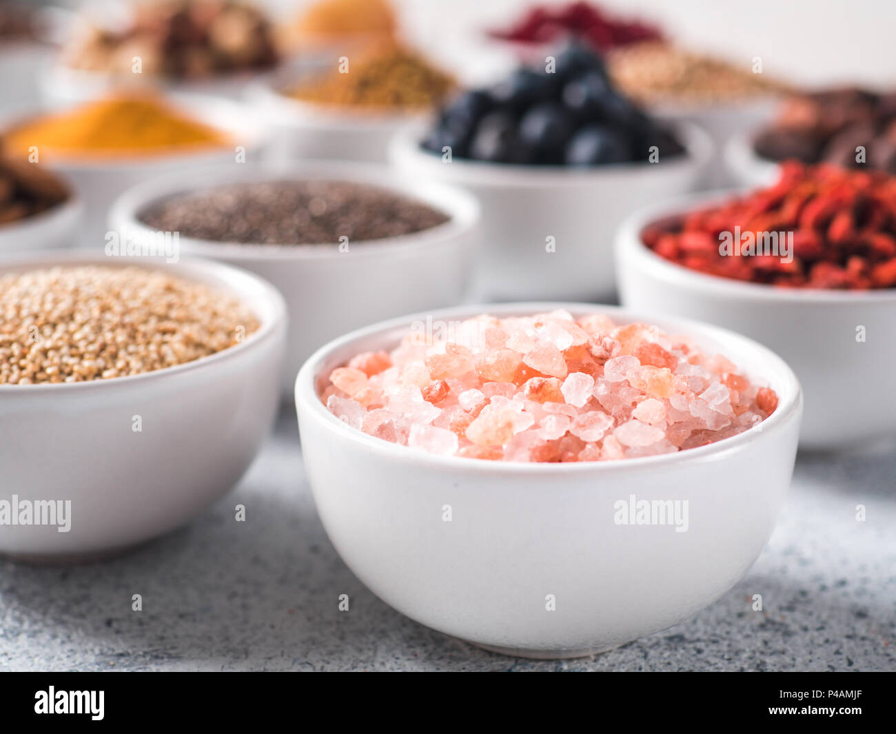 Sale rosa in piccola ciotola bianco e altri superfoods sullo sfondo. Messa a fuoco selettiva. Superfoods diversi ingredienti. Concetto e illustrazione per la super e detox food Foto Stock