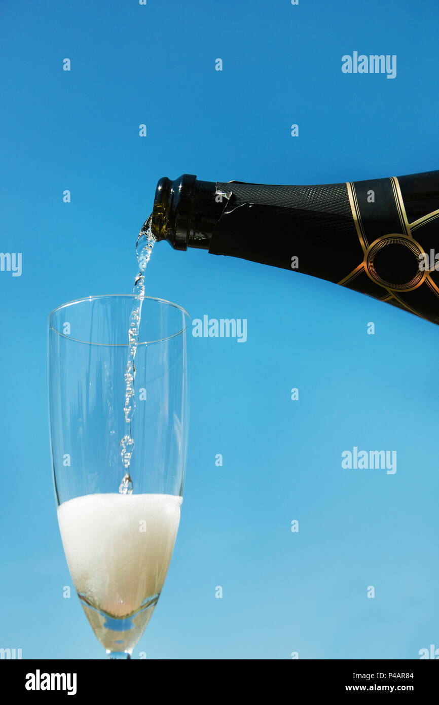 Versare lo champagne nel bicchiere contro il cielo blu sullo sfondo. Foto Stock
