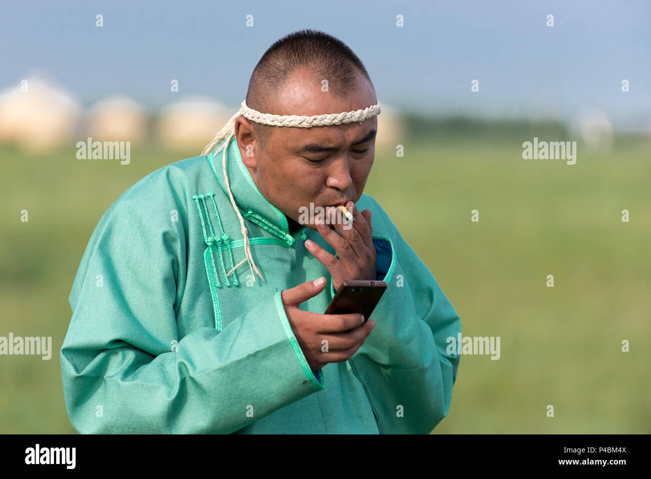 Un padre mongola fuma e controlla il suo smart phone al di fuori di un tempo estivo yurt, Zhenglanqi Wuyi, Mongolia Interna, Cina Foto Stock