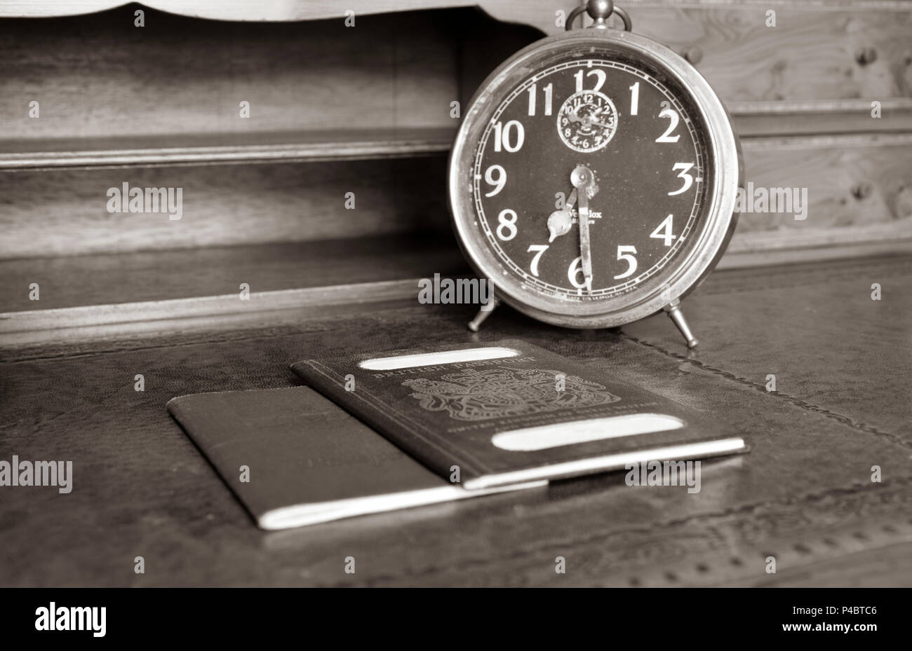 Blu di passaporto britannico e il passaporto australiano con il vecchio orologio sveglia su legni antichi scrivania in seppia Foto Stock