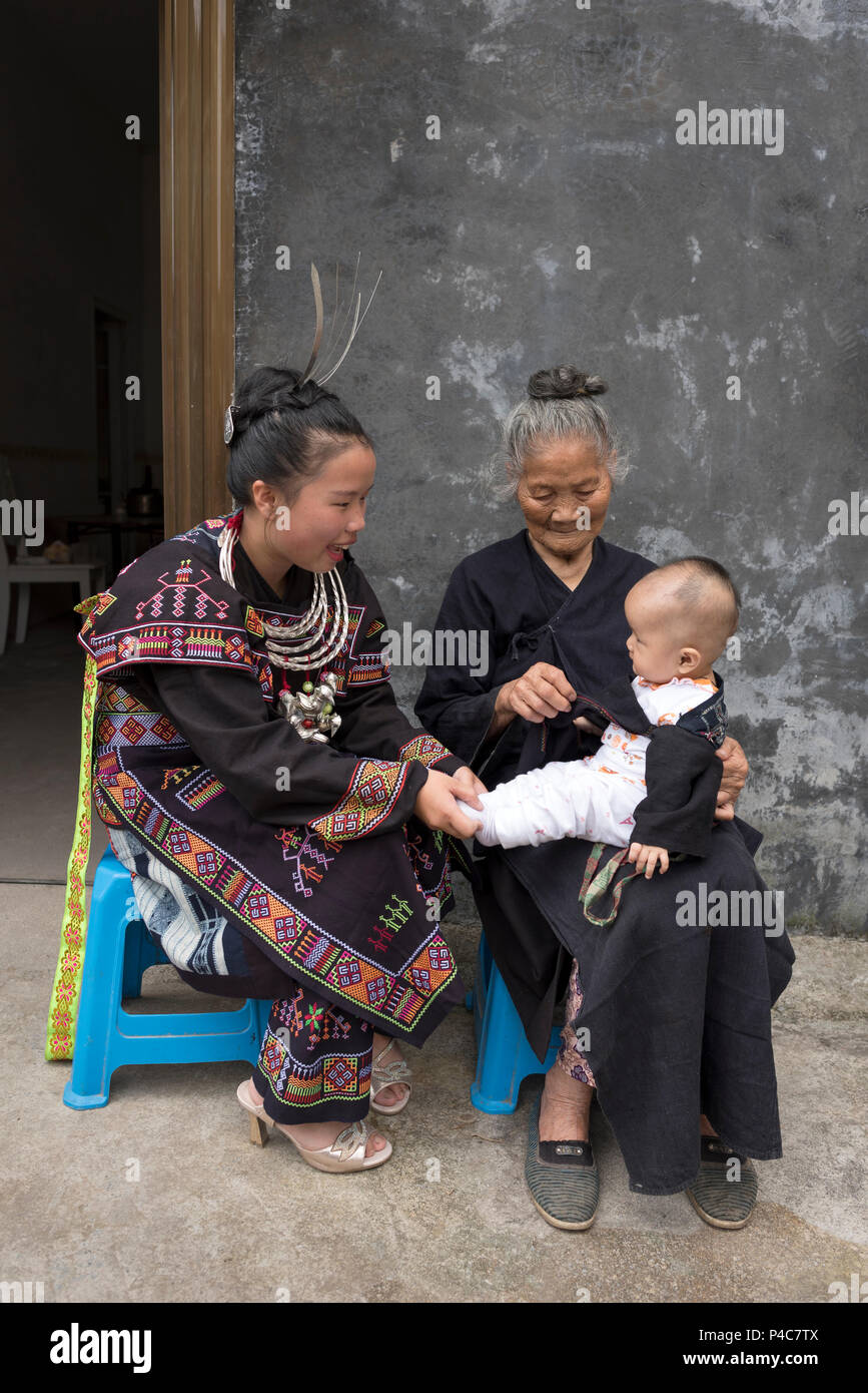 Mamma sorride al suo bambino che la nonna è holding, multi famiglia generazionale in costumi tradizionali, etnia Yao min Foto Stock