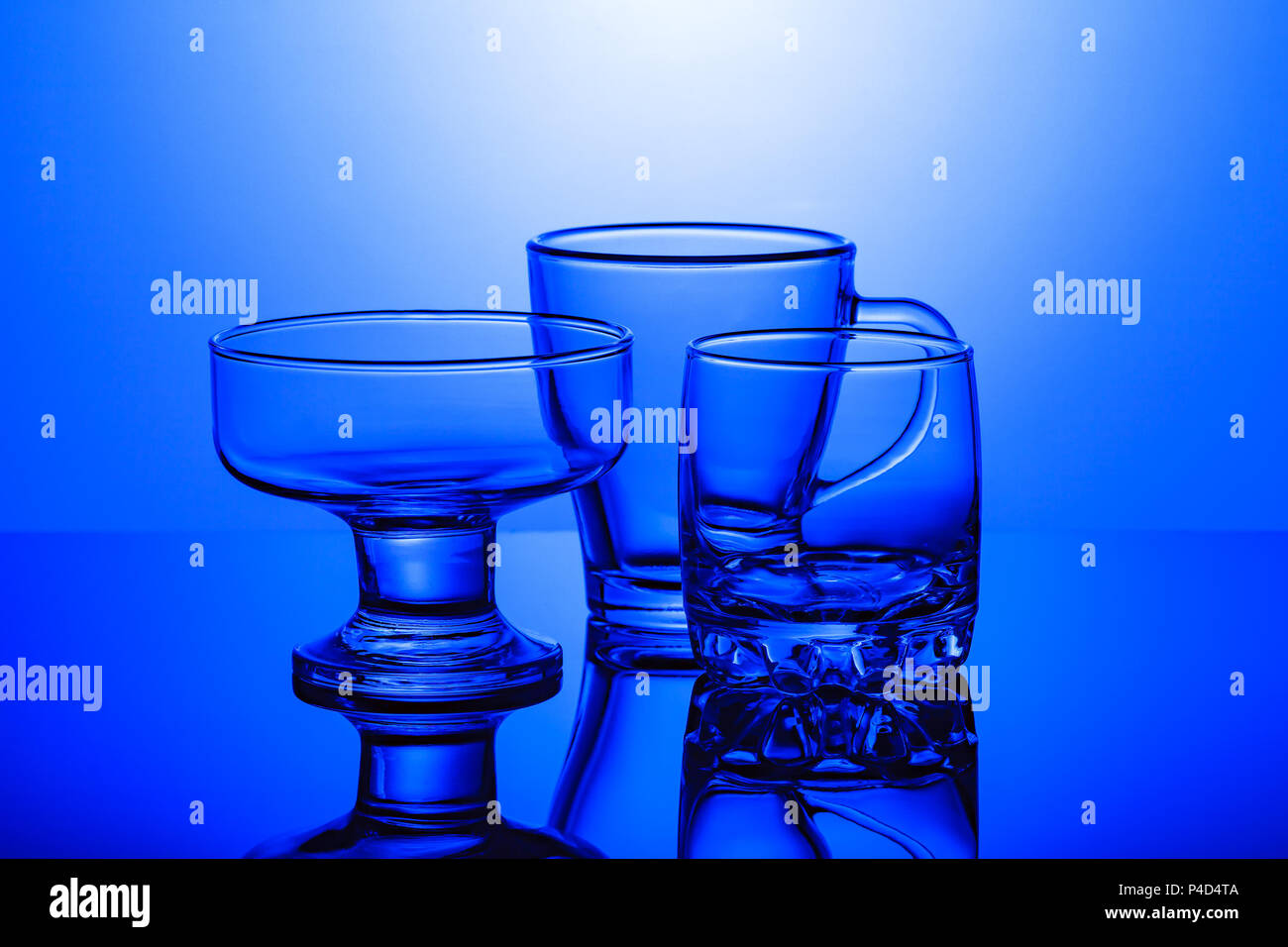 Vetro trasparente bicchieri stand su una superficie lucida su uno sfondo blu Foto Stock