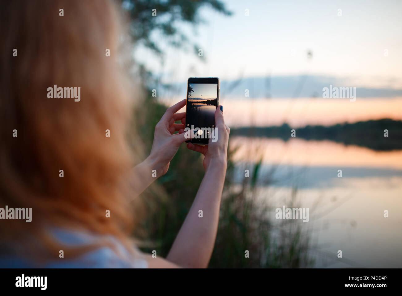 Donna che utilizza smartphone e prendendo la foto del tramonto colorato sopra il lago Foto Stock