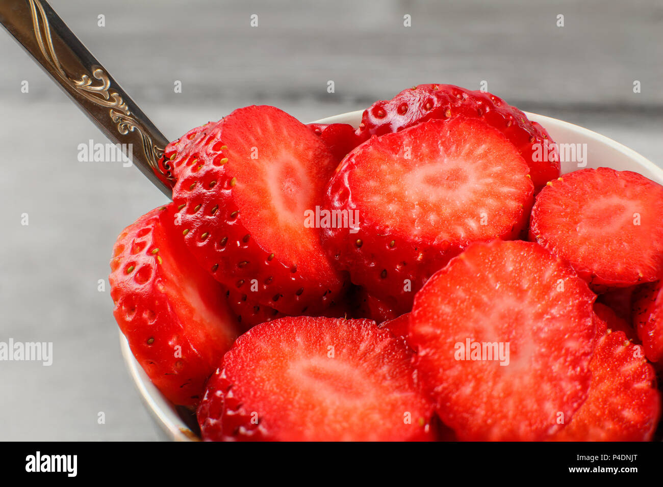 Dettagli su fragole tagliate in ambienti, in ceramica bianca ciotola con cucchiaio d'argento. Foto Stock