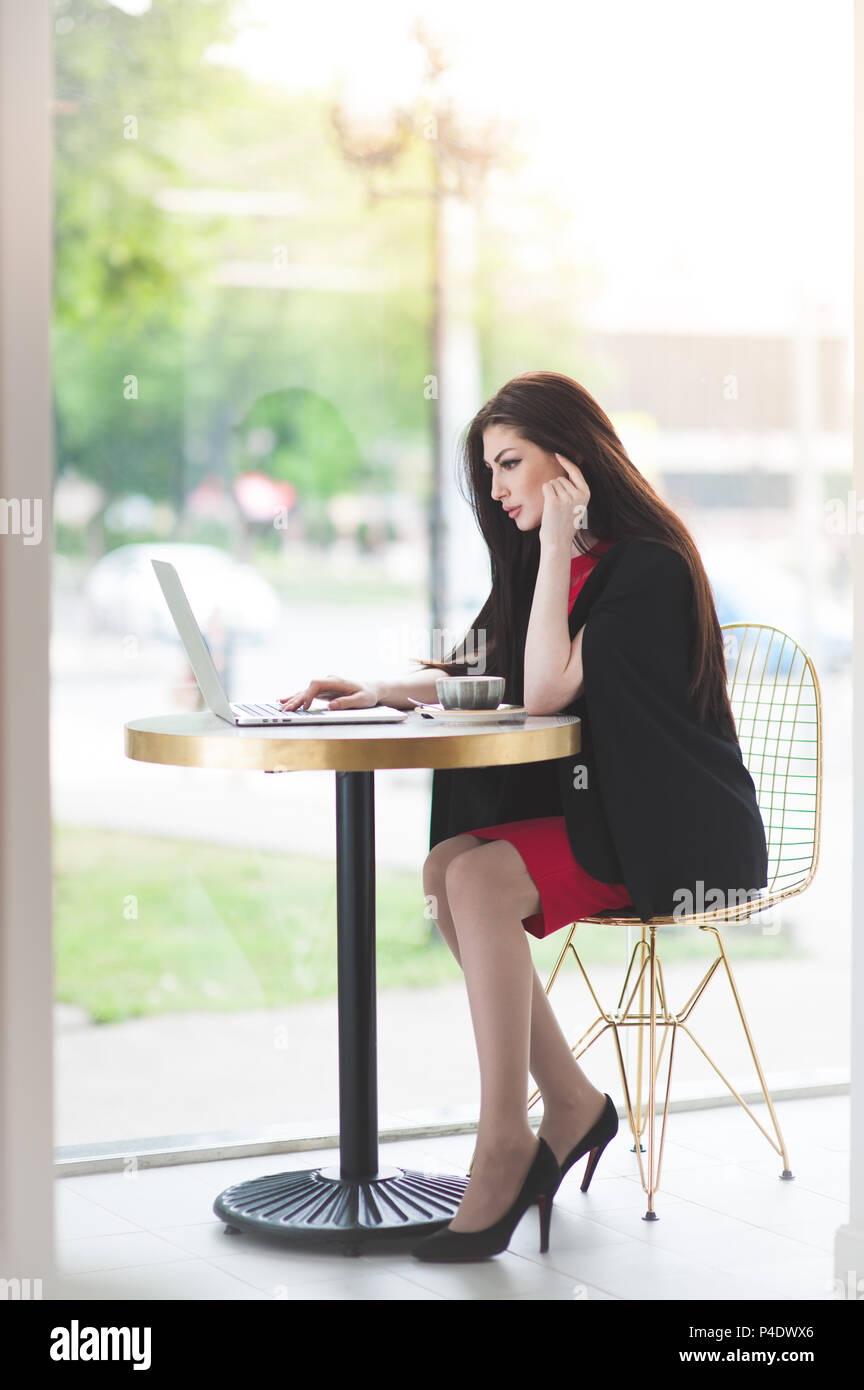 Bella ragazza elegante in nero costume rosso notebook di lavoro dietro la finestra nel cafe Foto Stock