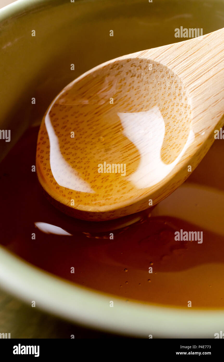 Close up di un cucchiaio di legno chiaro di sollevamento miele dorato dal verde vaso in ceramica. Foto Stock