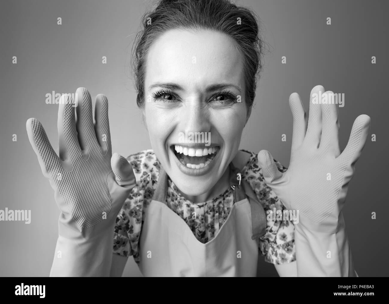 Grande tempo di pulizia. Sorridendo donna moderna in un grembiule che mostra i guanti di gomma sullo sfondo Foto Stock