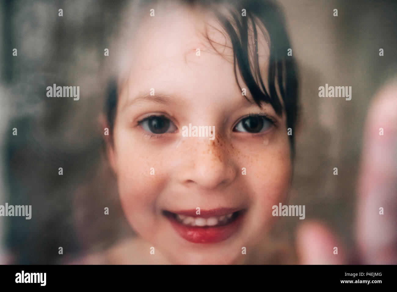 Ritratto di una ragazza sorridente guardando attraverso il bagnato vetro doccia Foto Stock