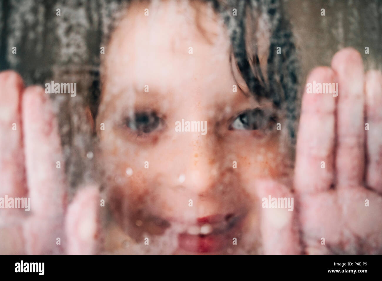 Ritratto di una ragazza sorridente guardando attraverso il bagnato vetro doccia Foto Stock