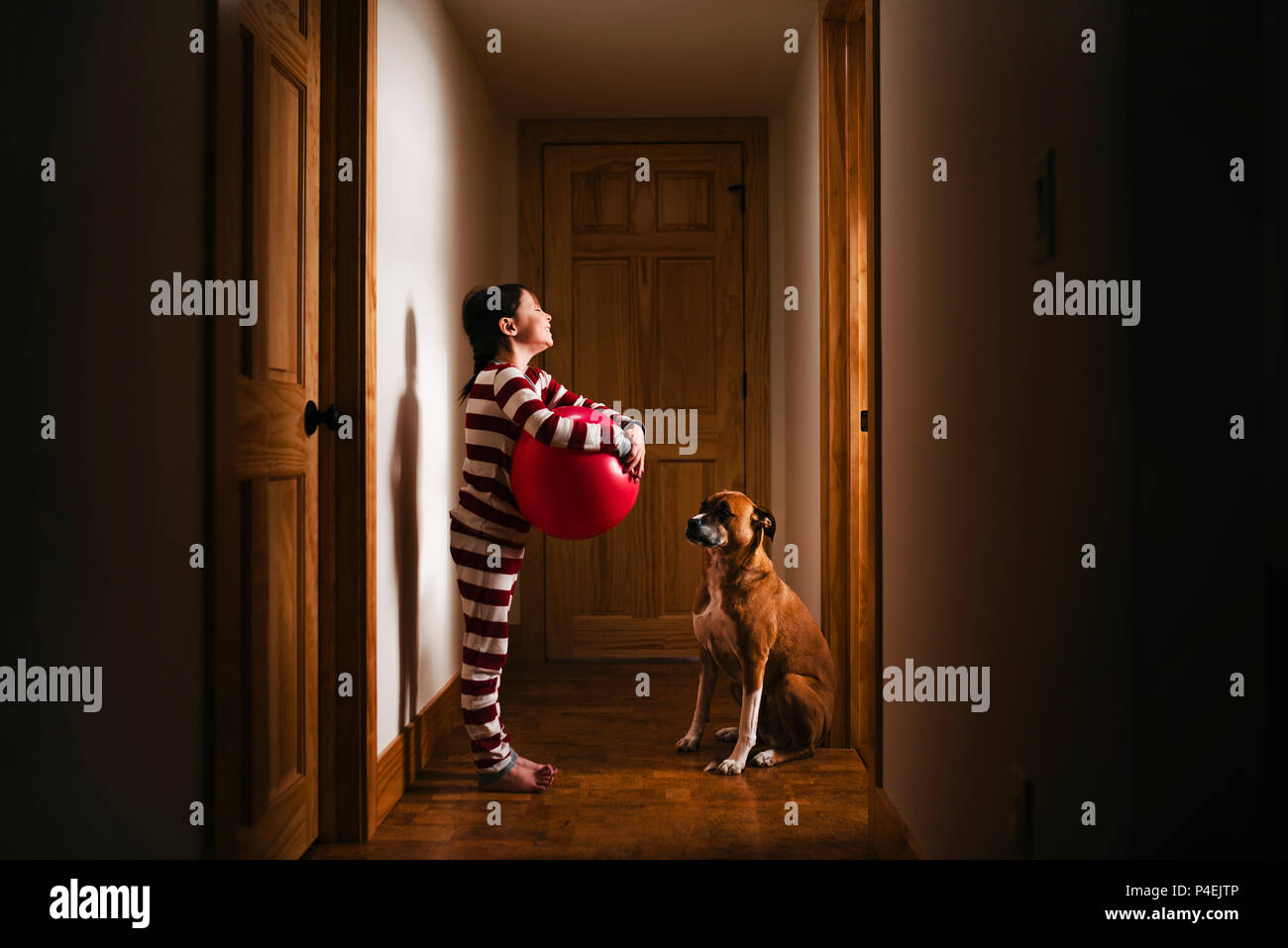 Ragazza in piedi nel corridoio tenendo una gigantesca sfera di gioco con il suo cane Foto Stock