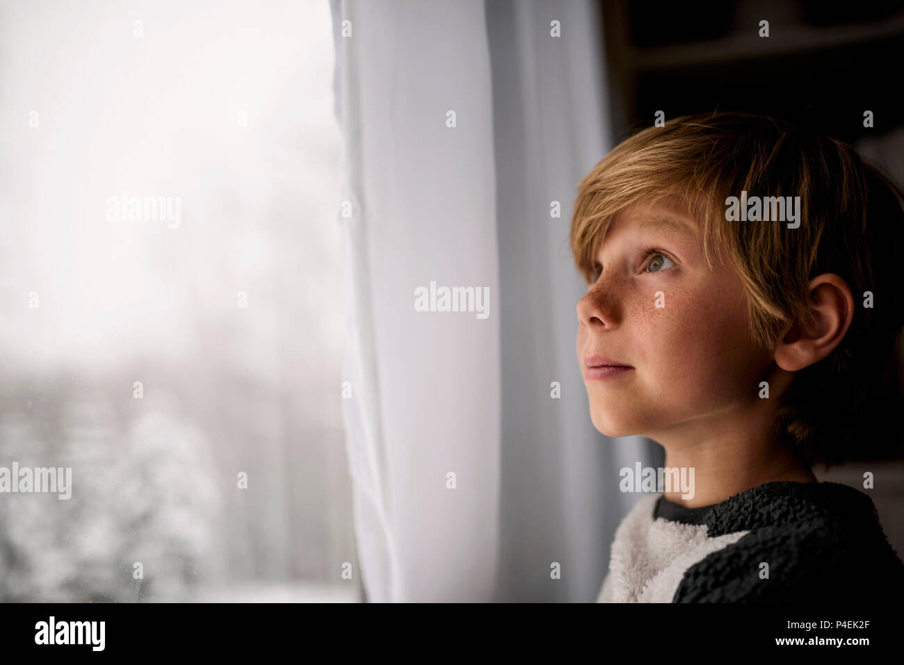Ragazzo che guarda fuori dalla finestra in inverno Foto Stock