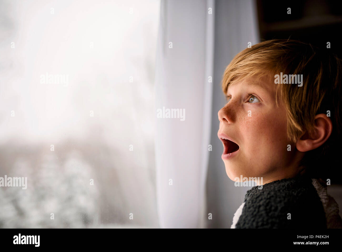 Ragazzo sorpreso guardando fuori della finestra in inverno Foto Stock