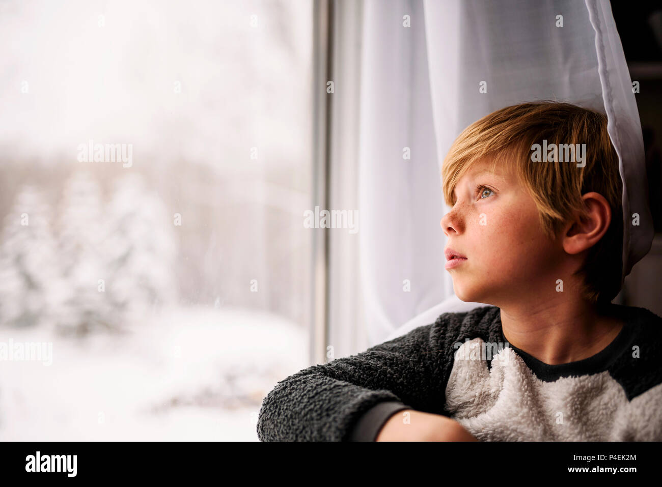 Ragazzo che guarda fuori dalla finestra in inverno Foto Stock