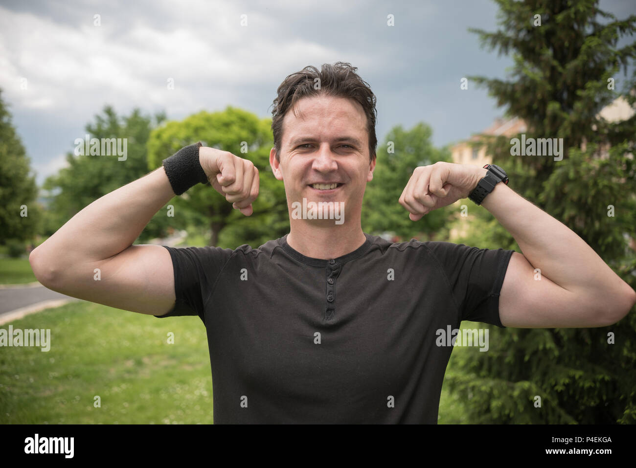 Uomo sorridente in piedi in flessione del parco i suoi muscoli Foto Stock