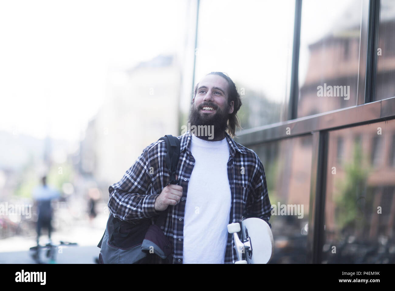 Uomo sorridente camminando per la strada che porta uno skateboard Foto Stock