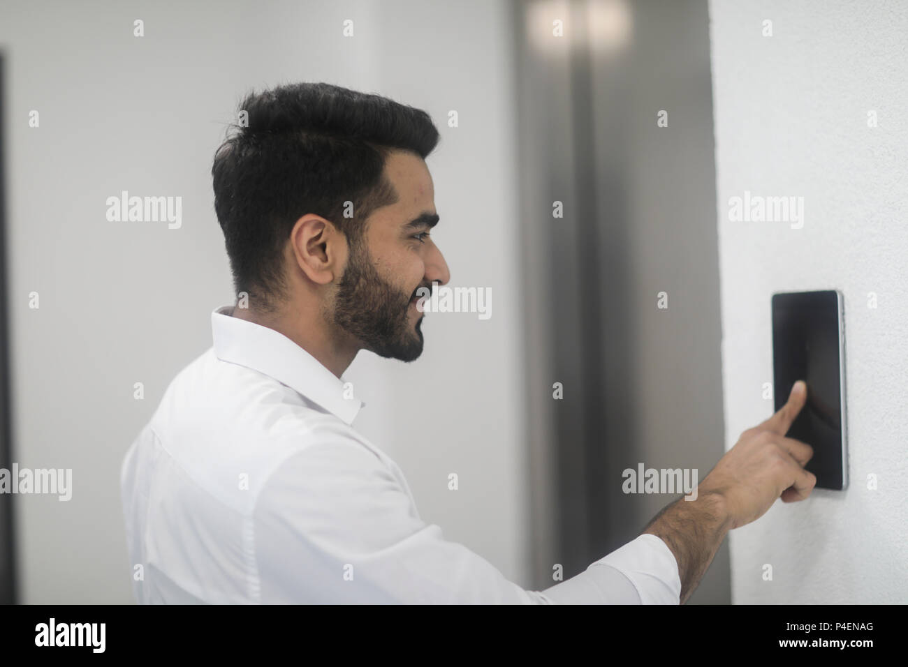 Uomo sorridente in piedi da un ascensore tramite il touch screen Foto Stock